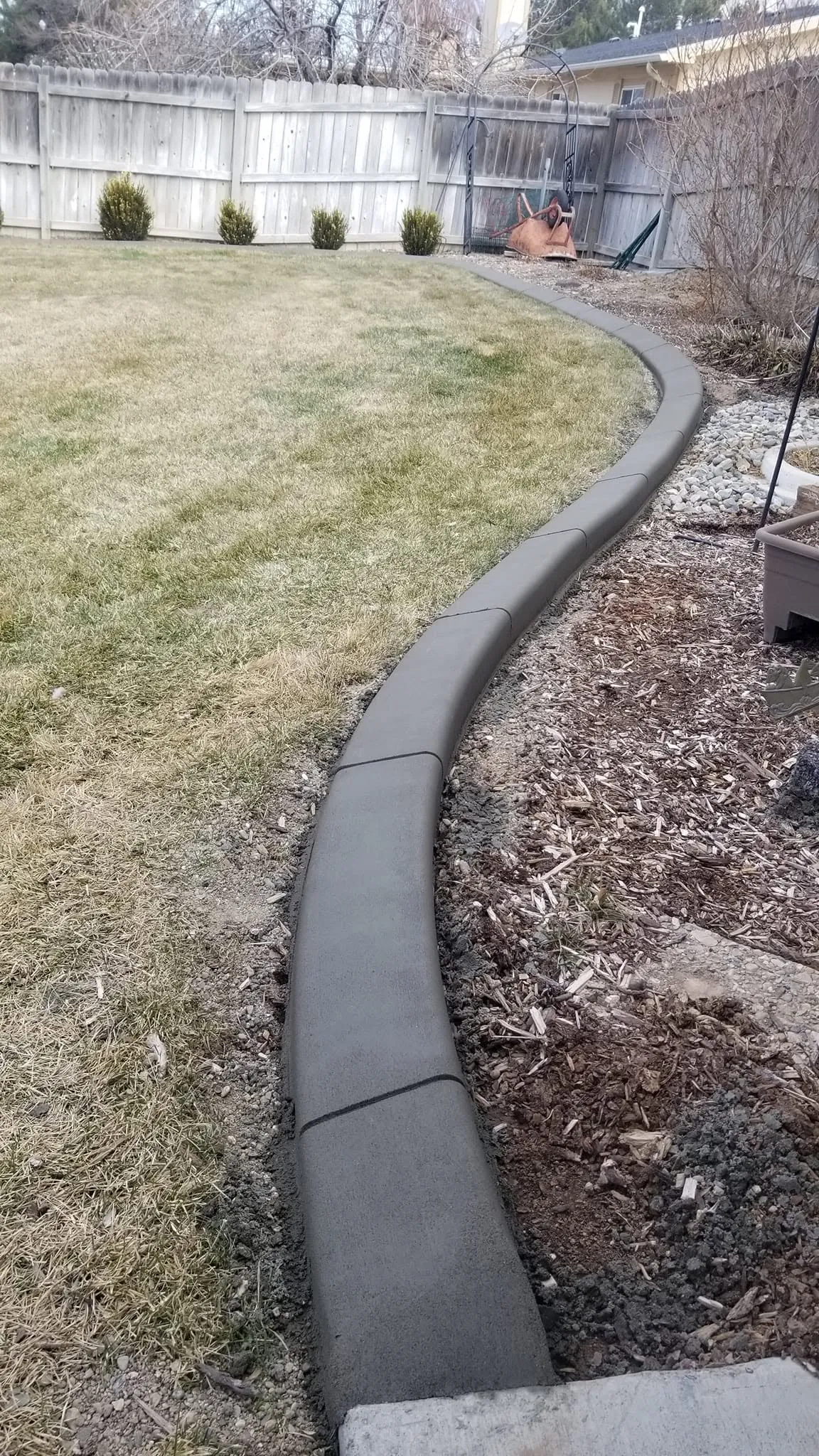 A dark gray curb follows a broad curve between lawn and a mulched shrub bed.