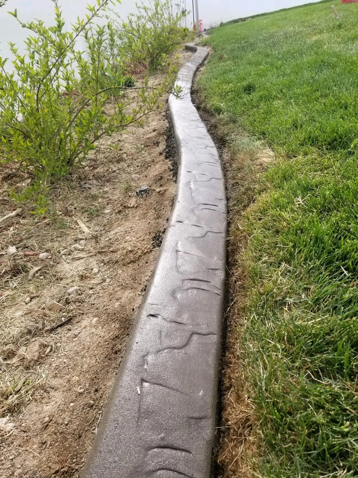 Close low-angle gray-brown stamped curb between a lawn and a planted soil bed.