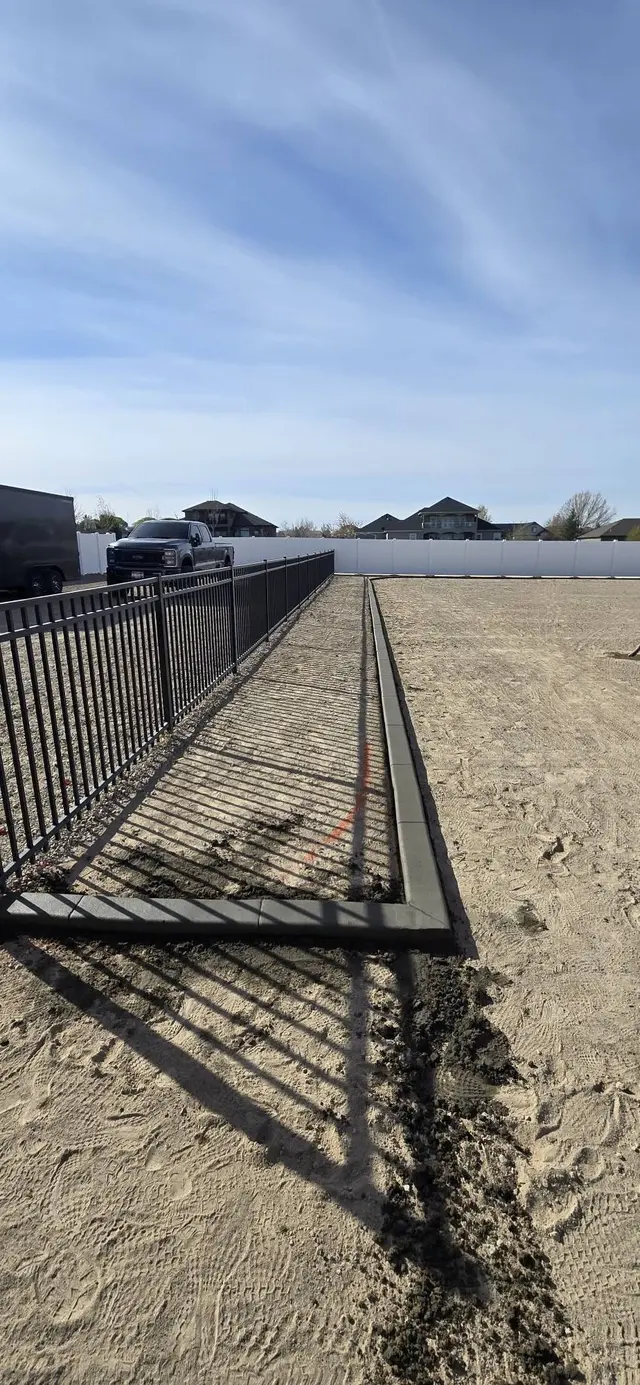 A long concrete border tracks alongside dark metal fencing.