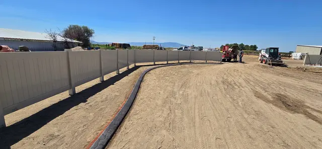 A dark stamped boundary follows a white fence across prepared ground.