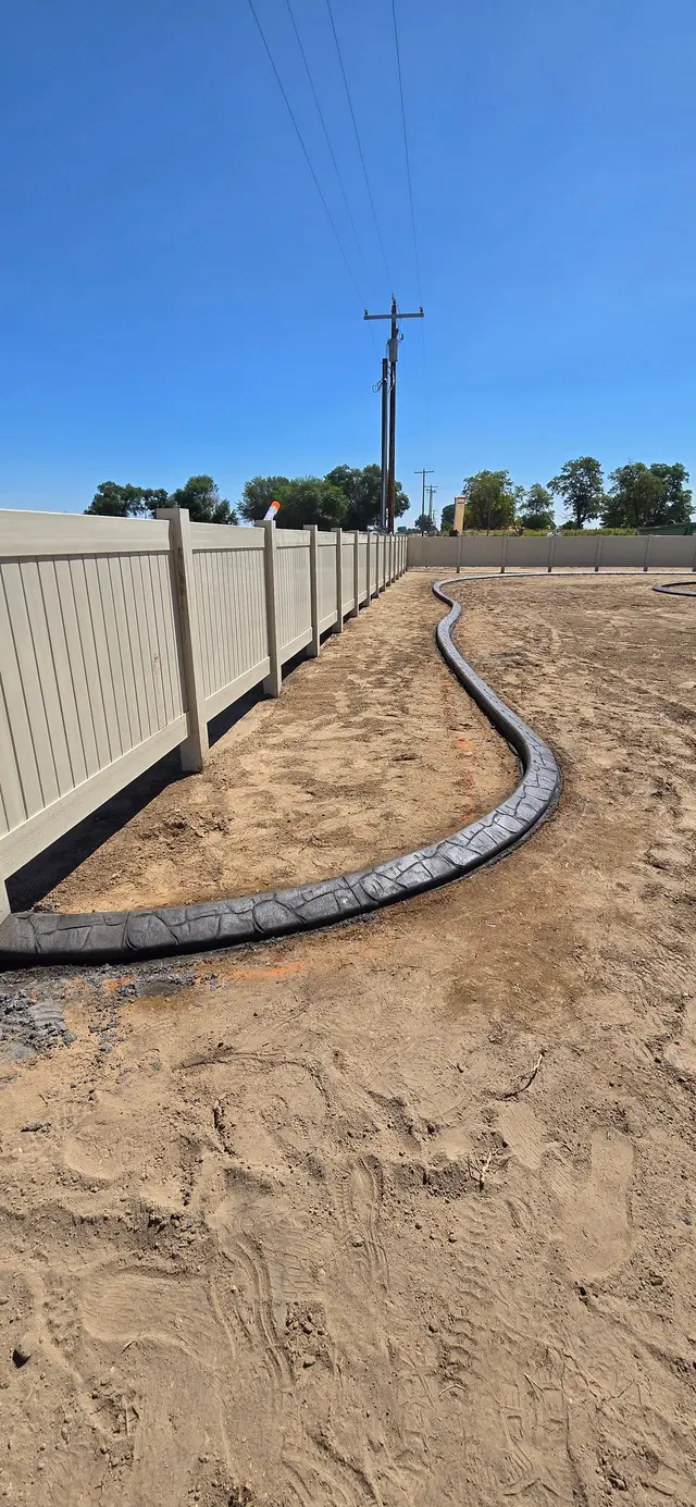 Stamped curbing leads along white fencing through a bare lot.