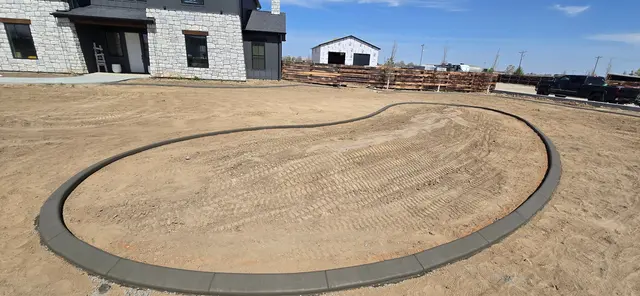 A fresh oval curb encloses a raked bed beside a modern house.