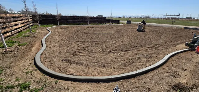 An organic-shaped fresh border follows a wood fence around bare ground.
