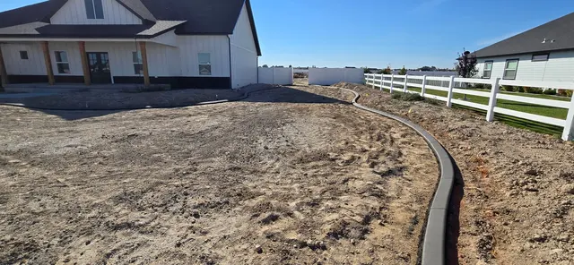 A long dark curve borders bare ground beside a house and white fence.