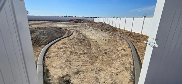 Two fresh concrete curves are viewed through an open white gate.