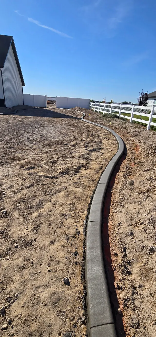 A close portrait shows a dark curved curb beside white fencing.