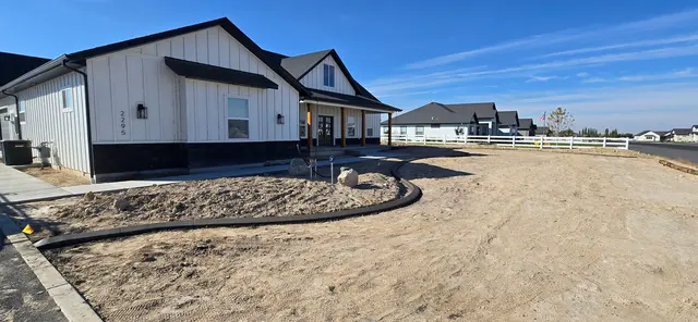 A fresh irregular border wraps the base of a house and a large boulder.