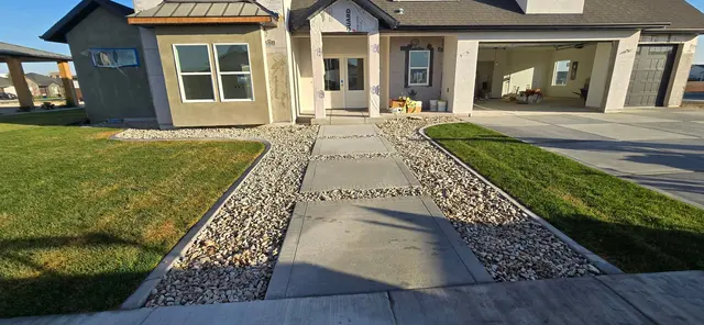 Parallel rock and concrete borders flank an entry walkway between green lawns.