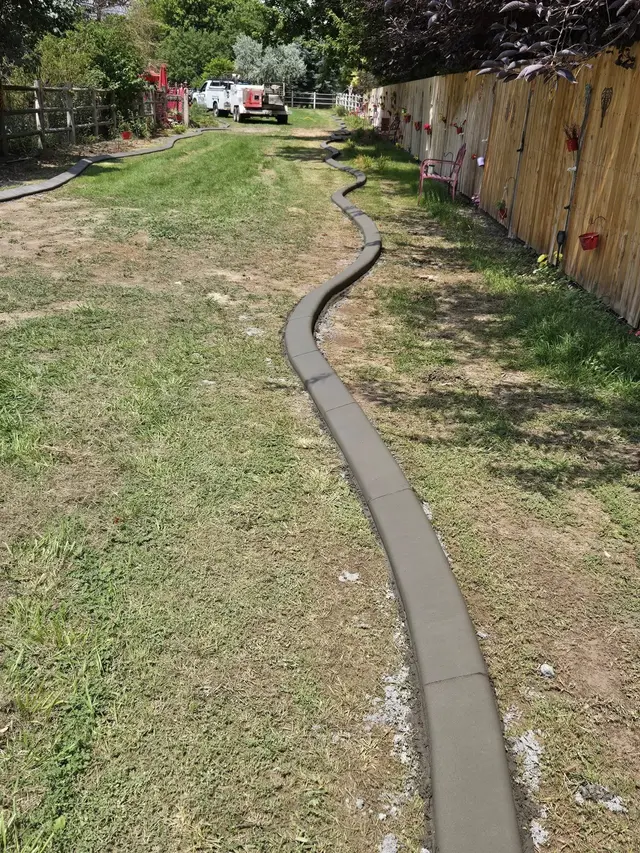 A single smooth curb winds beside a wood fence and lawn.