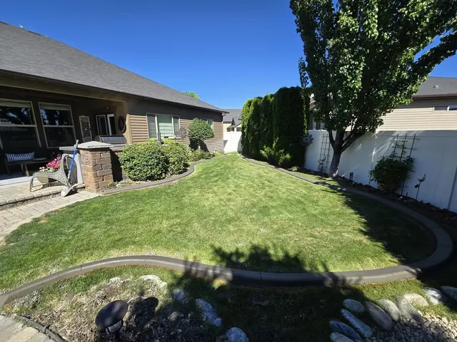 A curbed lawn is enclosed by house-side planting, trees and white fencing.