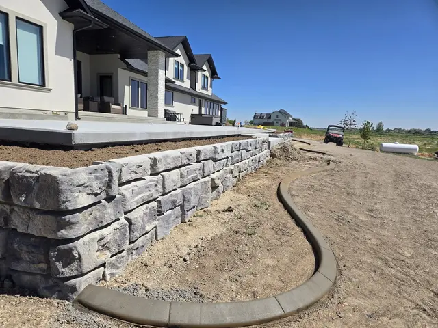 A fresh rounded curb closely follows the base of a stone retaining wall.
