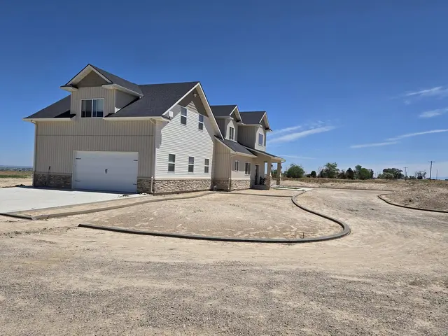 A long fresh border arcs across a bare lot beside a light-sided house.