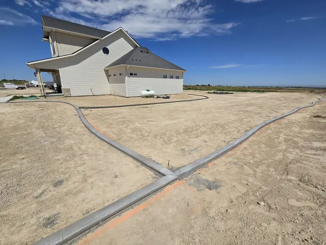 A straight concrete boundary meets a curved branch beside a house.