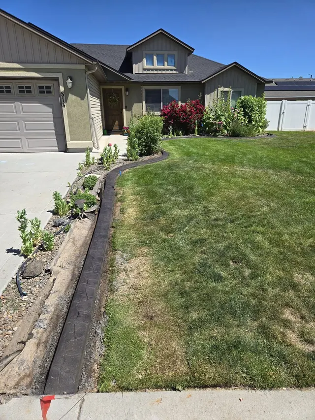 A pale curb borders a rock-and-shrub bed beside a driveway and lawn.