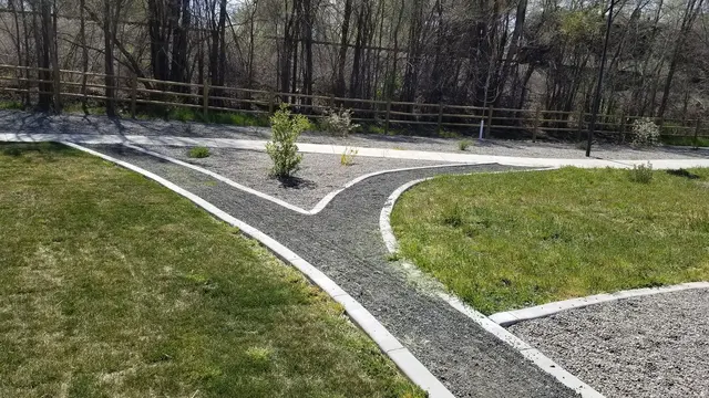 Pale concrete borders create a sharp-to-curved junction between gravel paths and lawn.