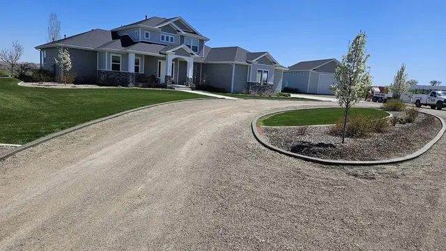 A flowing concrete border defines a planted island in a gravel drive beside a broad lawn and house.