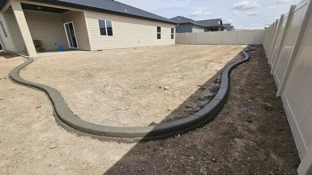 Fresh gray curves wrap a prepared backyard along a white fence and house.