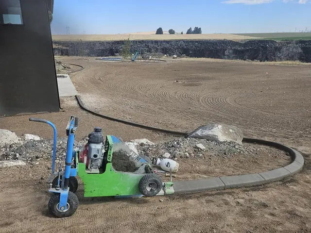 A green curbing machine sits beside newly installed curves and rock beds.