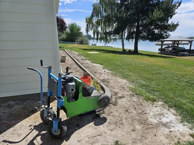 A green curbing machine stands beside a fresh curved house-side bed and lawn.
