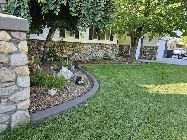 A dark curb sweeps between lush lawn and flowers below a stone-faced house.