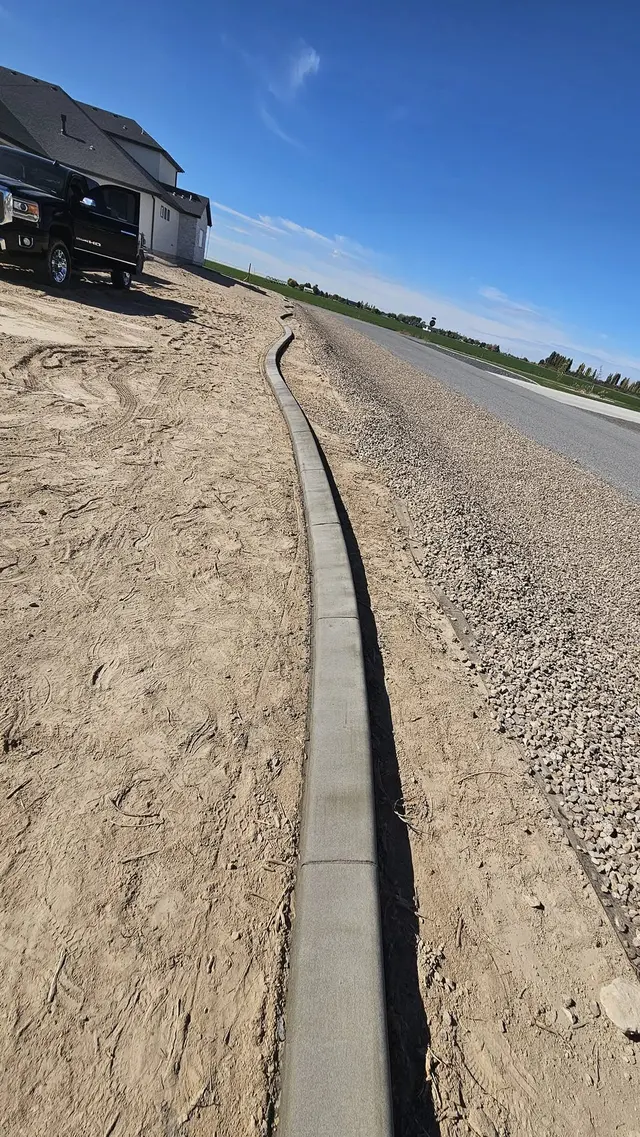 A portrait view follows a new concrete border along an unplanted roadside strip.