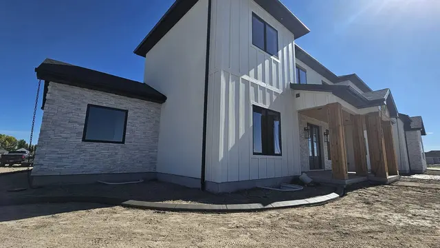 A low concrete edge follows the front wall of a house against blue sky and bare soil.
