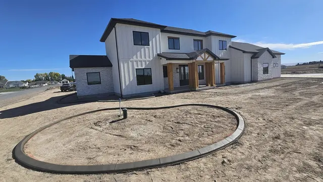 A circular concrete planting border stands in freshly graded soil in front of a house.