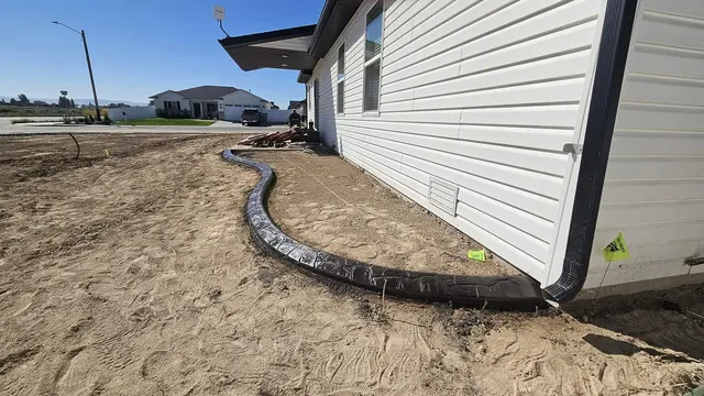 A dark textured border sweeps around a house foundation through graded soil.