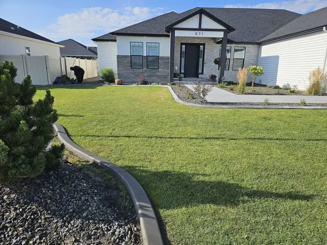 A gray garden border leads through a finished lawn toward a house and pale gravel beds.