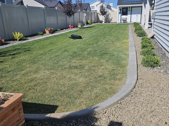 A smooth gray border separates a green side lawn from a narrow gravel planting strip.