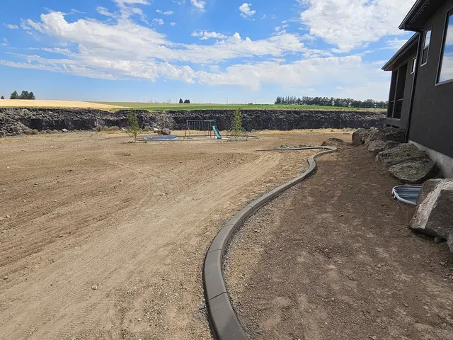 A fresh concrete edge follows a sweeping line beside a house through a graded yard.
