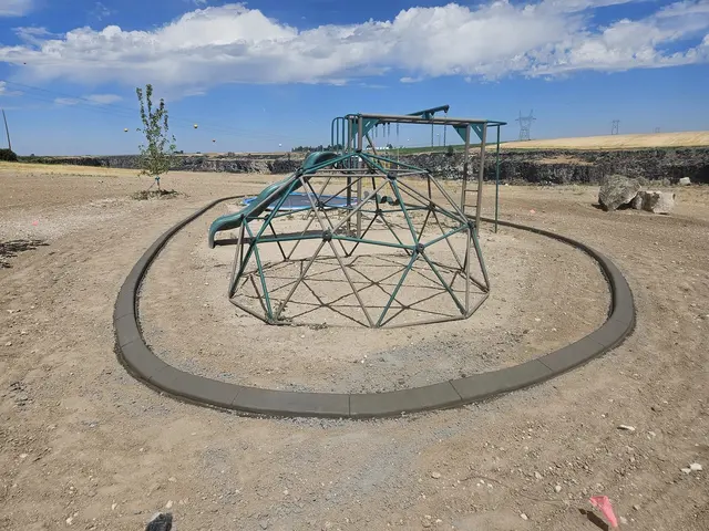 A broad concrete ring encloses a metal climbing frame on a bare yard.