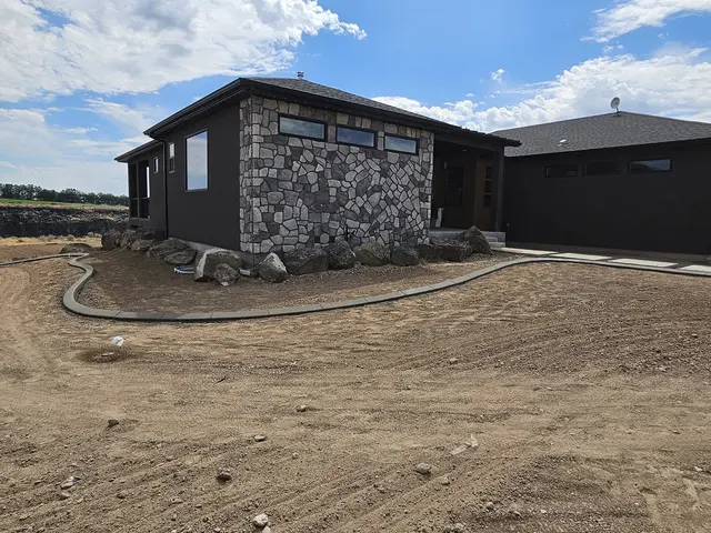 A fresh concrete border rounds the corner of a house with a stone-clad front wall.