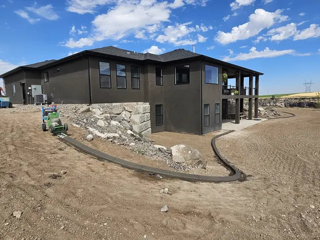 A gray concrete edge flows around large boulders below a dark modern house.