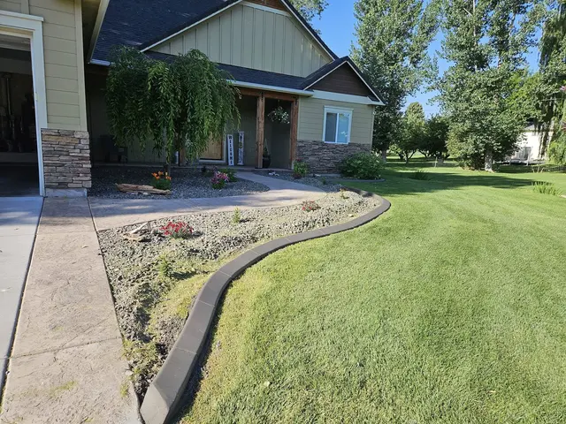 A sweeping gray edge separates a green lawn from a pale planting strip beside a porch.