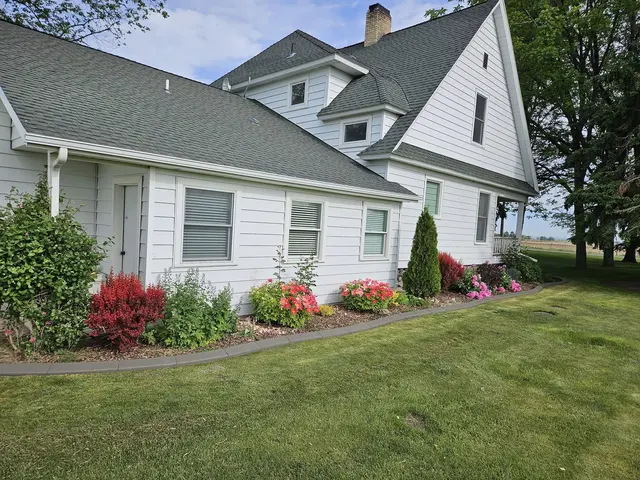 A gray border separates a green lawn from colorful planting along a white house.