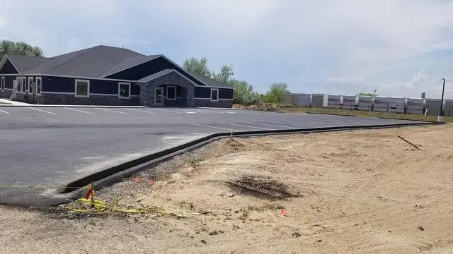 A dark concrete edge follows the perimeter of a paved area with bare soil alongside it.