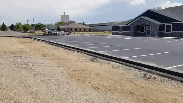 Long straight curb borders a striped commercial parking lot and low office building.