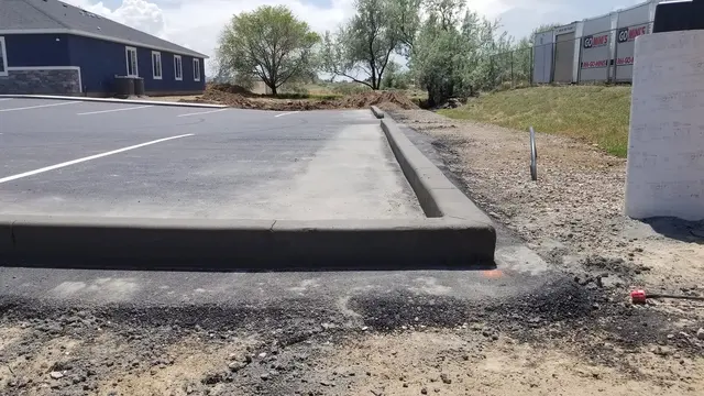 A dark concrete curb forms a crisp right-angle corner beside a marked paved surface.
