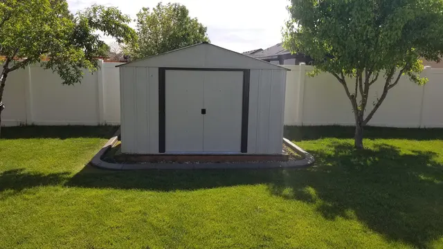 A low concrete edge neatly encloses the base of a shed on a green lawn.