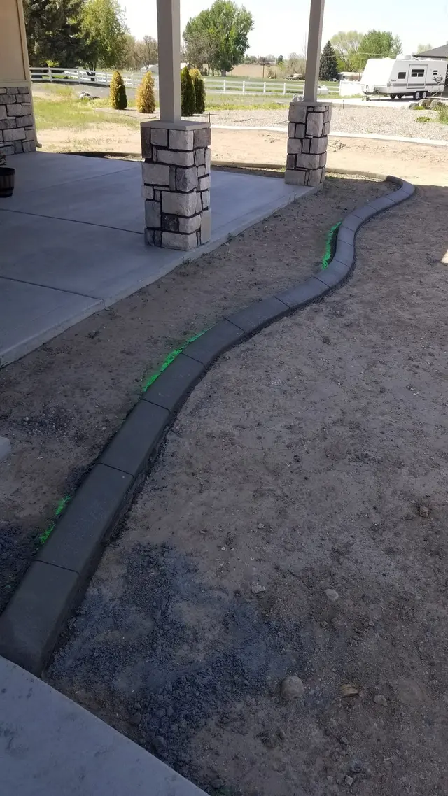 A portrait shows a new curb following the perimeter of a covered patio beside bare soil.
