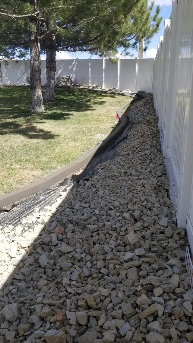 A narrow stone strip and gray curb run alongside a white fence under trees.