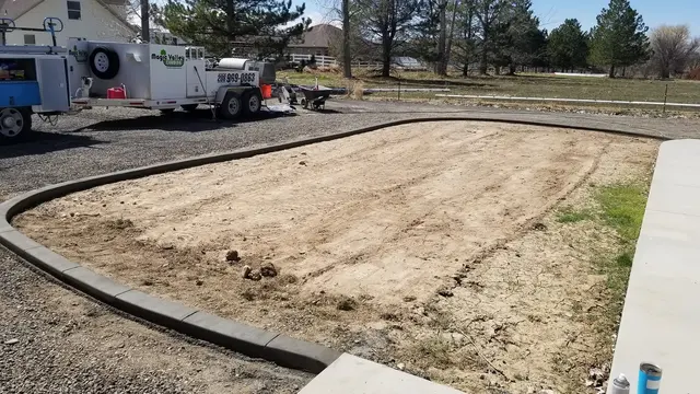 A concrete border outlines a wide bare bed beside a walk with company equipment behind it.