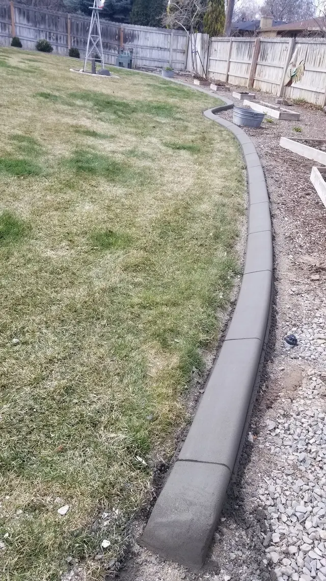 A gray border separates patchy lawn from a mulched foundation strip beside a house.
