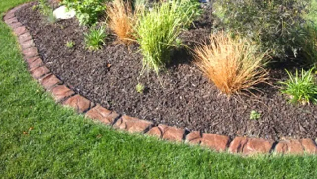 A close horizontal view follows a reddish textured curb around a mulched garden bed.