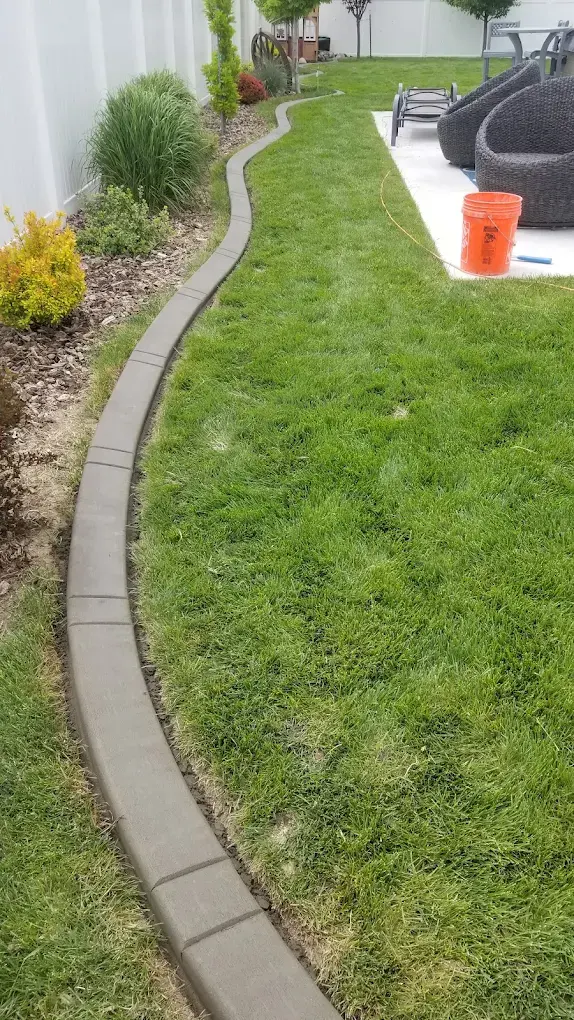 Narrow view of a fresh gray curve between lawn and a shrub bed along a white fence.