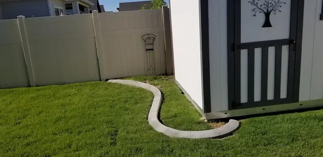 Small S-shaped concrete border curves around a white and dark-trimmed shed.