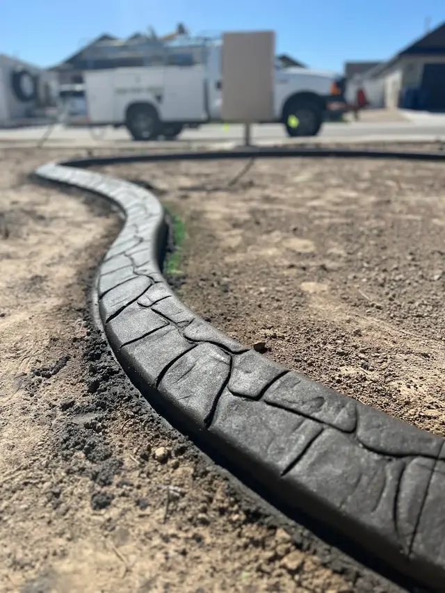Close low-angle view of a dark stamped concrete curve with a new-build worksite softly blurred behind.