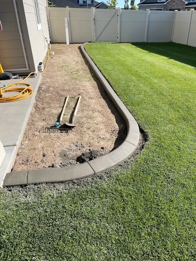 Fresh dark curb forms a narrow bed between a house and lawn, with hand tools inside.