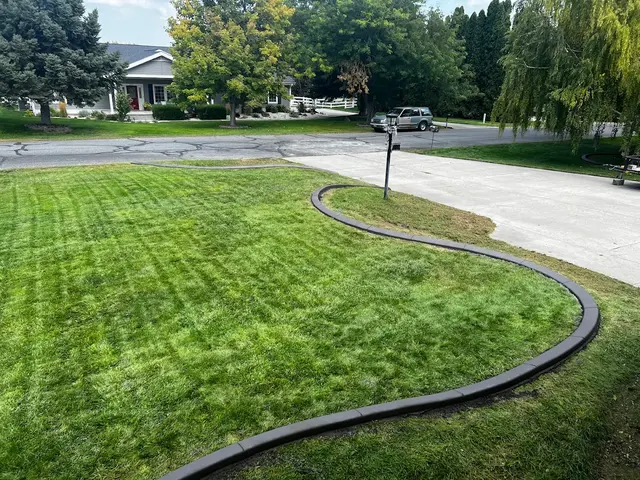Broad S-shaped dark curb defines a neatly mown front lawn beside a driveway and mailbox.
